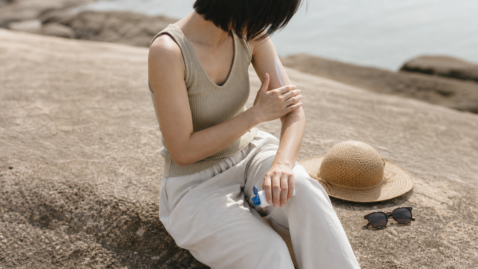 女士在陽光下補搽防曬霜，旁邊放有遮陽帽和太陽眼鏡。