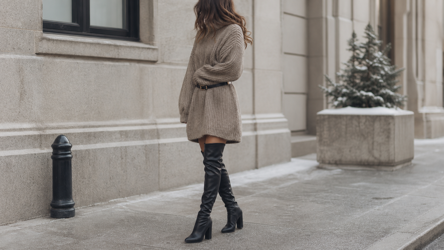 A woman in an oversized sweater dress paired with tall leather boots on a winter street.