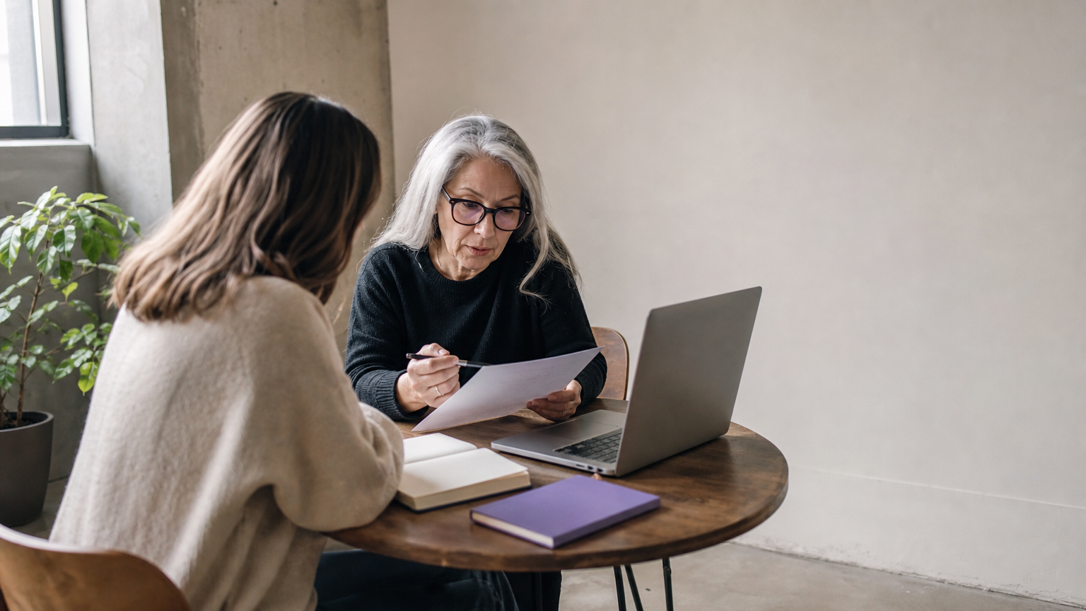 A senior PR consultant reviews a press release with a business owner at a small table.