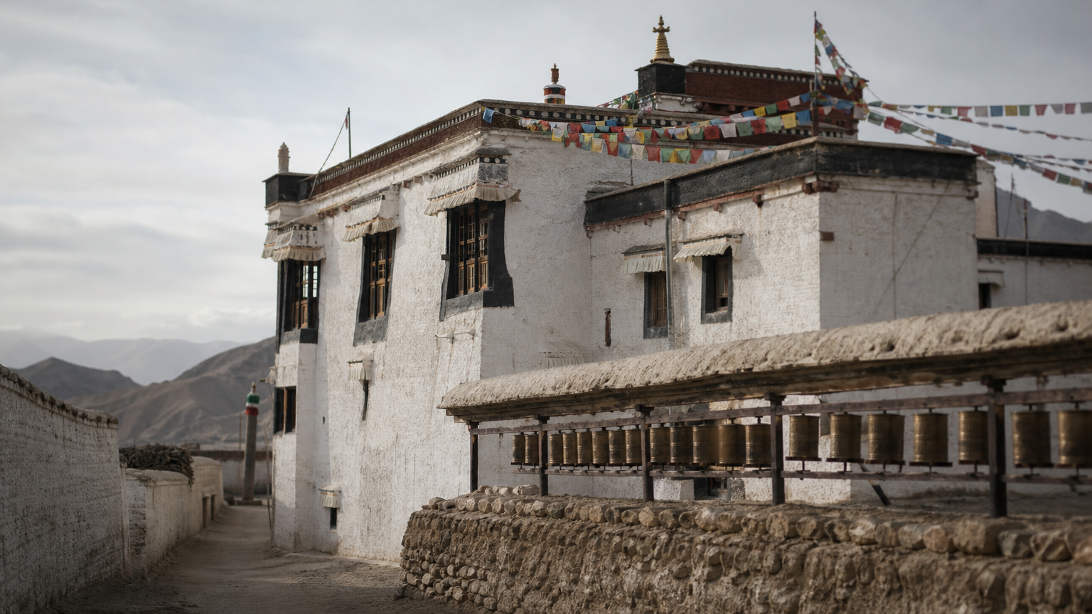 Whitewashed monastery inside a walled desert town with prayer flags and a row of prayer wheels.