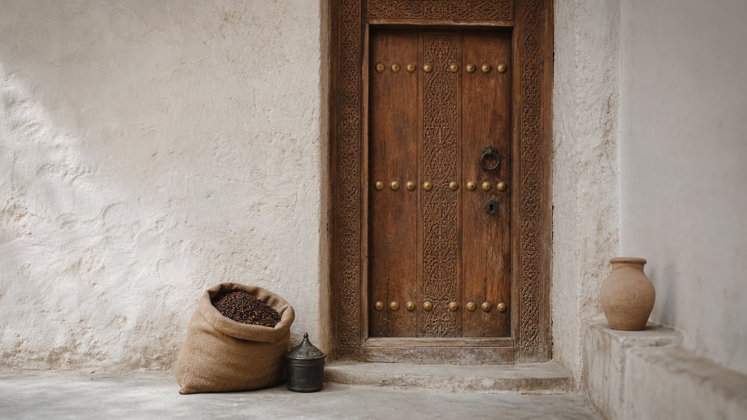 A carved wooden door with brass studs set in a whitewashed wall.
