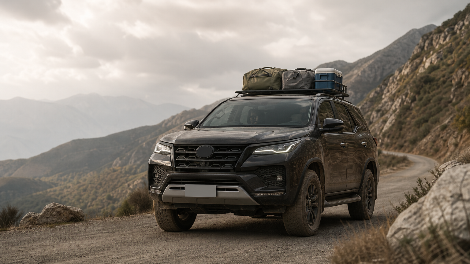 A Toyota Fortuner SUV climbs a winding mountain road with luggage on its roof rack.
