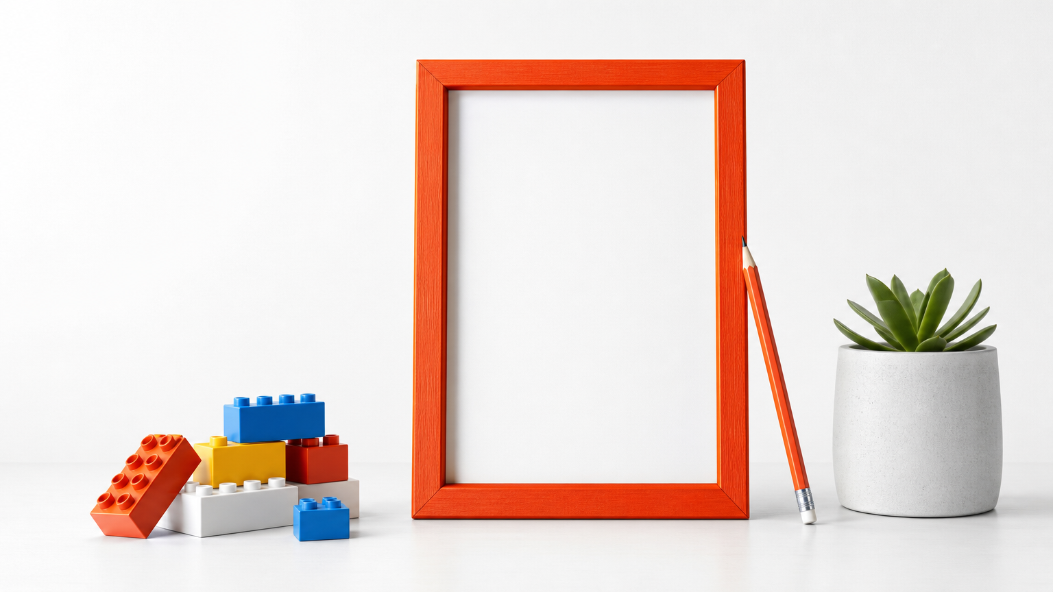 An empty picture frame stands on a tabletop beside a stack of building blocks and a pencil.