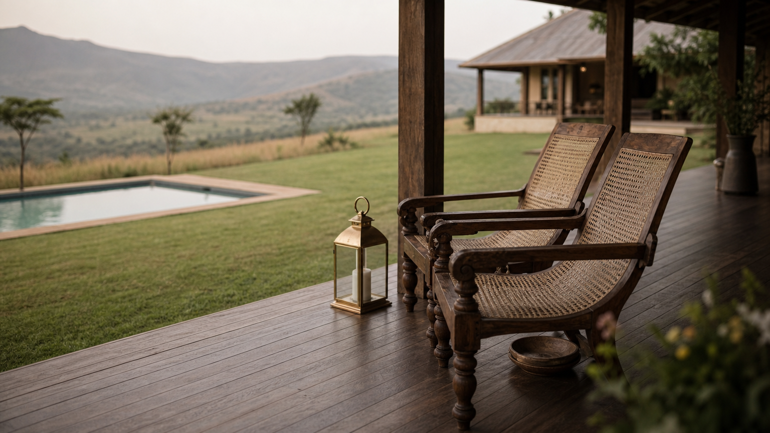 A hilltop homestead with a deep veranda, carved chairs, a lawn and a view across grassland to distant hills.